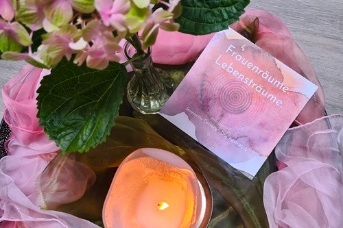 Arrangement mit Kerze und Blumen und dem Flyer Frauenräume.Lebesnträume in rosatönen