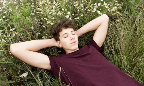 junger Mann liegt mit geschlossenen Augen auf einer Blumenwiese
